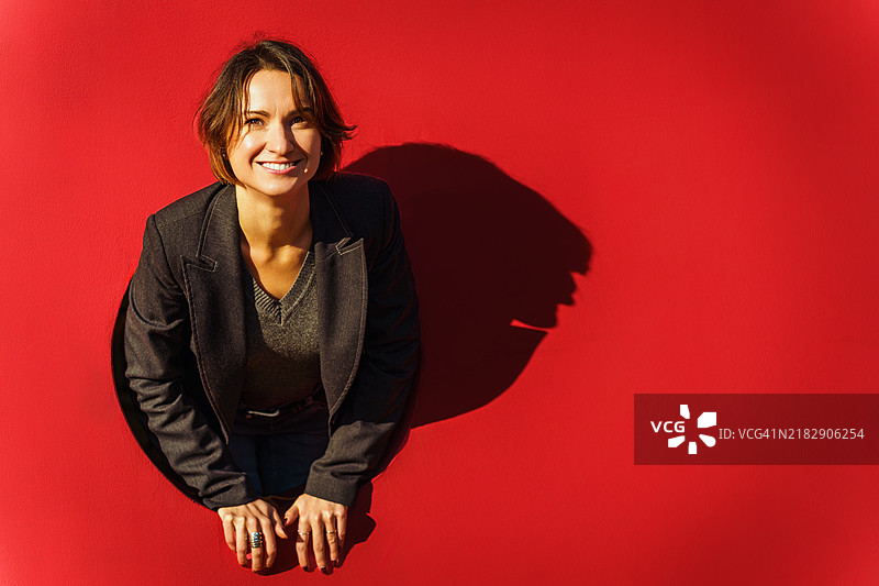 快乐的年轻女性透过红色墙壁的洞窥视图片素材