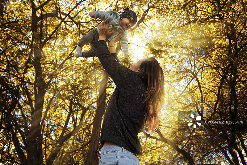 母亲在日落的森林中将儿子高高举起。图片素材
