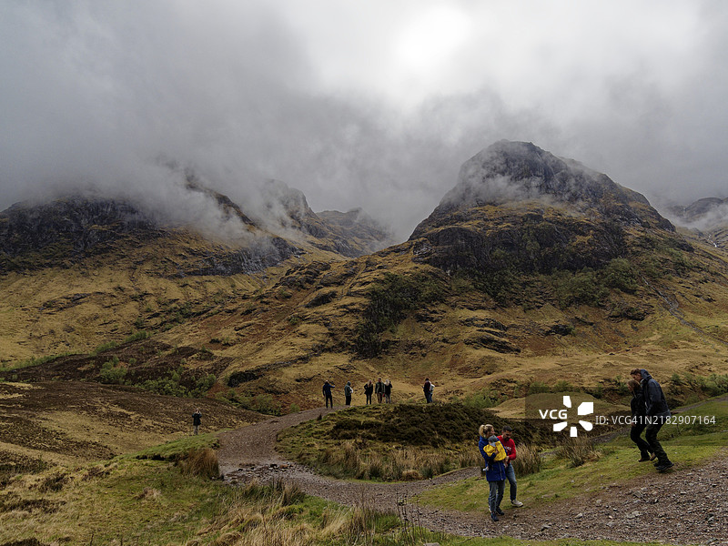 在苏格兰大不列颠的三姐妹山前，雾气缭绕的山地风景中，人们驻足欣赏。图片素材