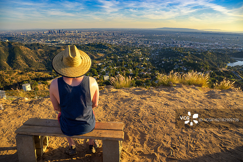 背影男子坐在长椅上，背景是城市风景图片素材