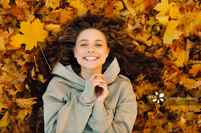 微笑的年轻女性躺在森林中的秋叶上图片素材