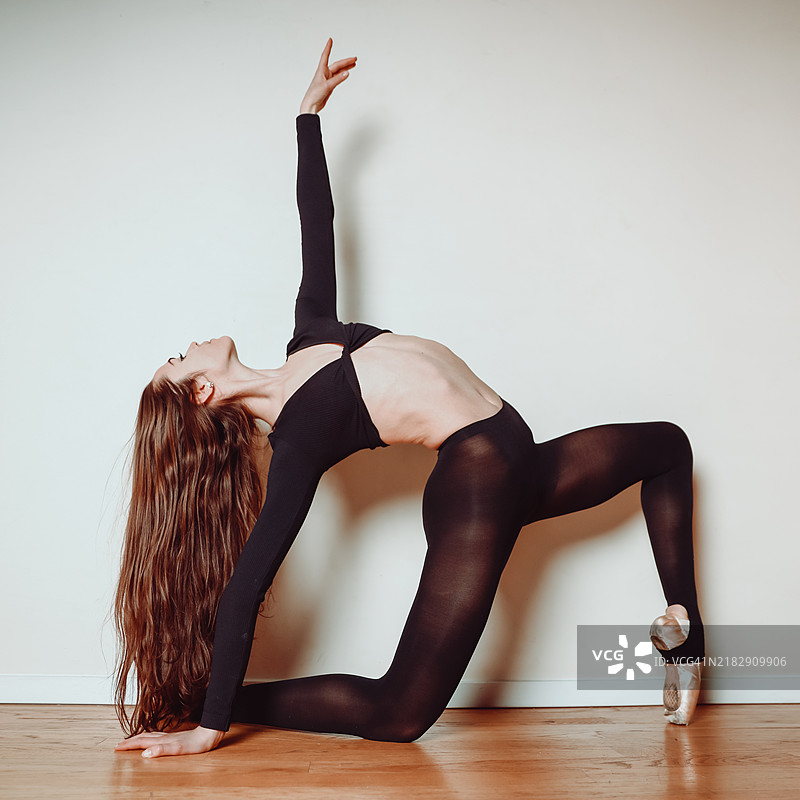 侧面视图的灵活舞者穿着黑色紧身裤，摆姿势于白色墙壁前，芝加哥，伊利诺伊州，美国图片素材