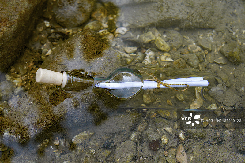 漂浮在海岸岩石上的水中瓶子里的信息图片素材
