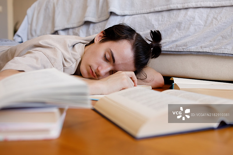卧室地板上，正在学习书籍的年轻男孩沉沉入睡的肖像图片素材