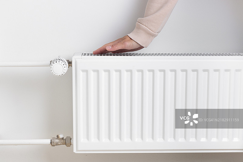 女人在家中靠近暖气散热器取暖，寒冷季节的资源管理图片素材