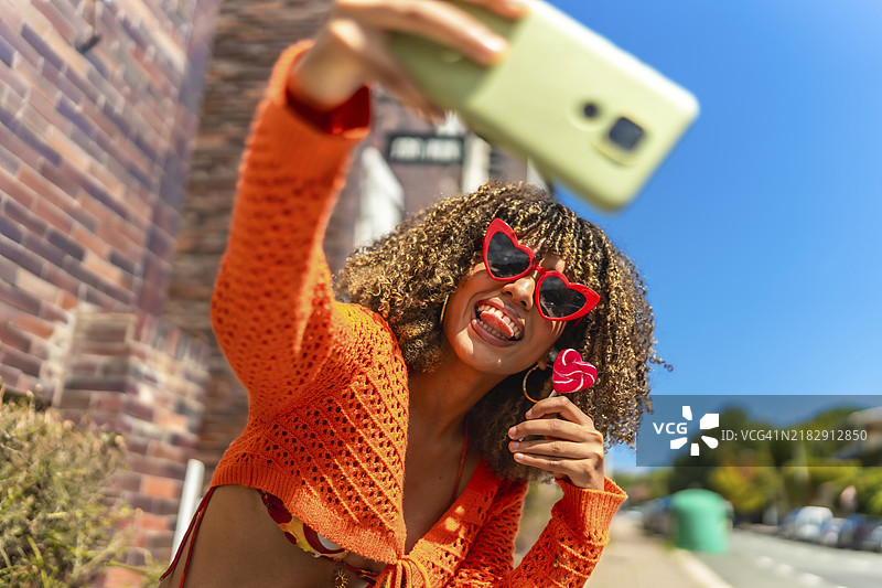 年轻充满活力的拉丁裔女性在户外吃棒棒糖时自拍图片素材