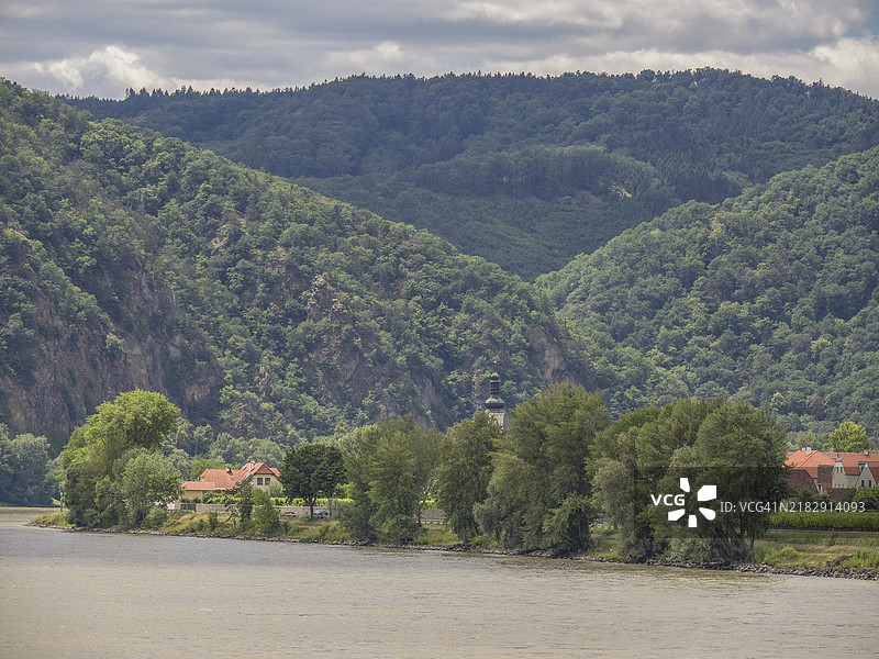 多瑙河畔的郁郁葱葱的植被和背景中的森林山丘，杜尔斯坦，瓦豪，奥地利，欧洲图片素材