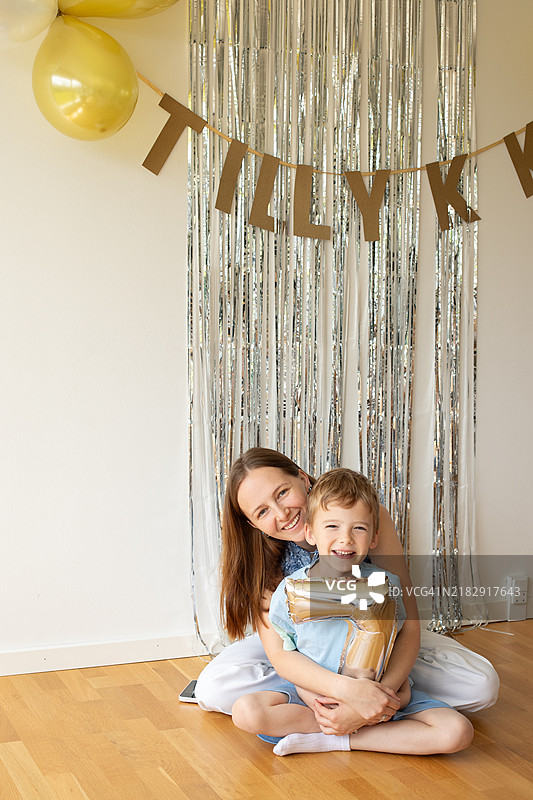 快乐的母亲和儿子坐在家里的地板上庆祝生日图片素材