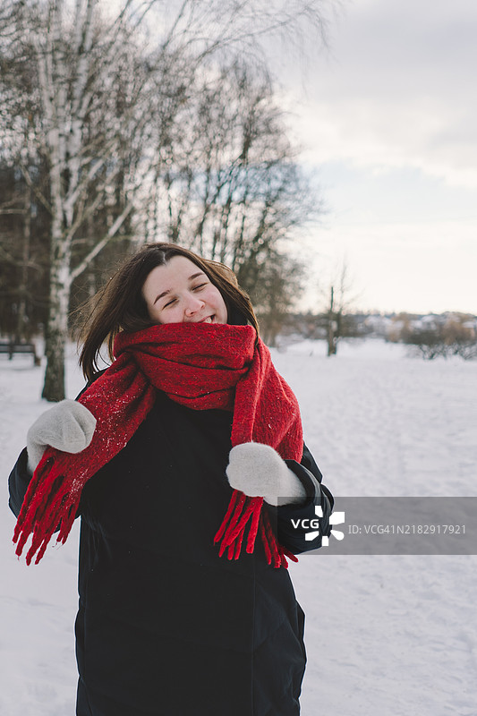 一位戴着红色围巾的女性在阳光明媚的蓝天下，享受着森林中的雪白冬日。图片素材