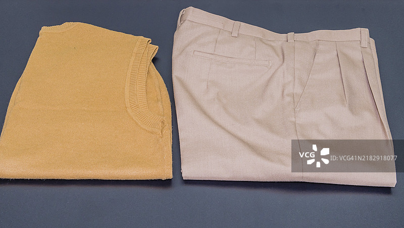 棕色无袖毛衣与一条米色褶皱裤子放在黑色背景上图片素材