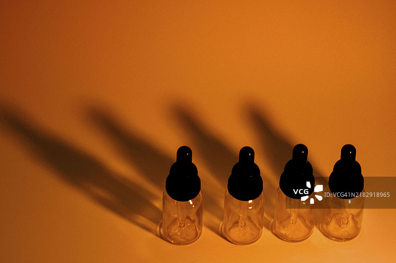 四个玻璃滴管瓶在金橙色背景上投射出深黑色阴影。为了效果添加了一些噪音。图片素材