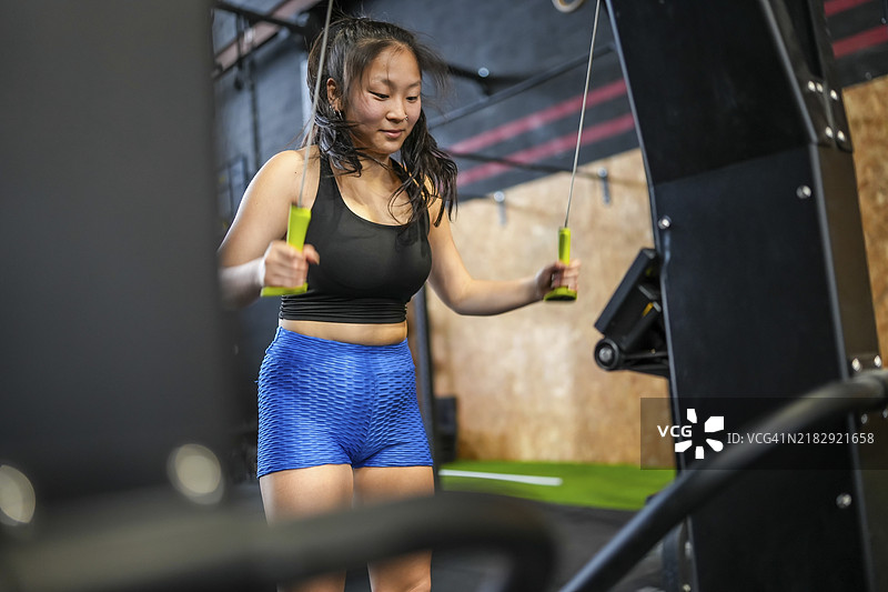 强壮的中国女性在交叉训练健身房使用背阔肌训练器拉重物锻炼。图片素材