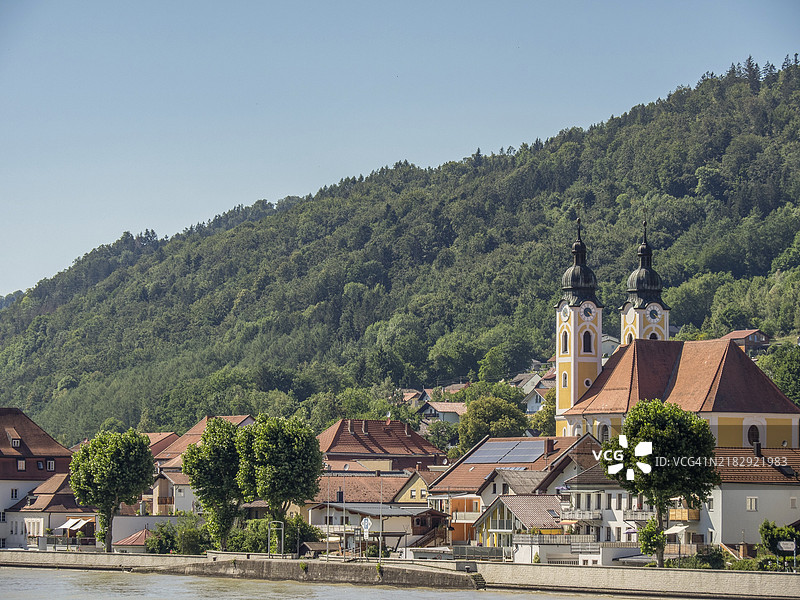 奥地利瓦豪地区的杜恩斯坦，河岸边的乡村村庄，有教堂建筑和房屋，四周环绕着绿色的山丘和森林。图片素材