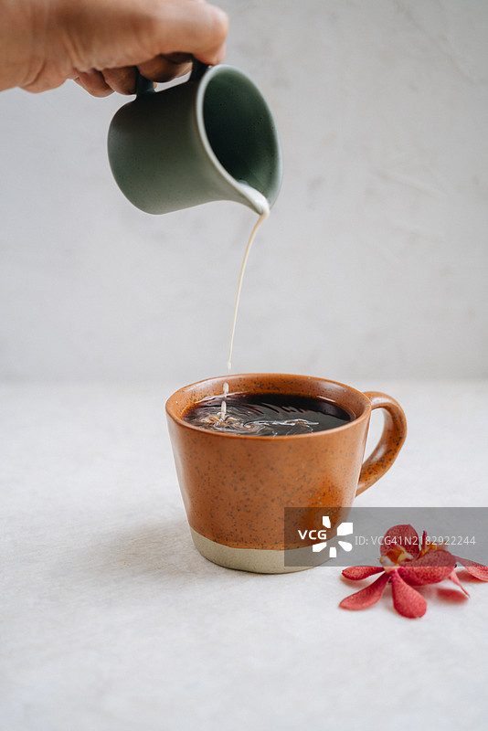 女性的手在桌子上将牛奶倒入热美式咖啡中图片素材