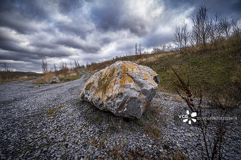 令人印象深刻的大石头位于砾石小径上，背景是多云的天空，地点为Oetelshofen采石场，Schöller，伍珀塔尔，贝尔吉施地区，北莱茵-威斯特法伦。图片素材