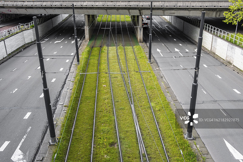 铁路轨道下方有绿色草坪，穿过一座桥，两侧是空旷的道路，鹿特丹的电车轨道。图片素材