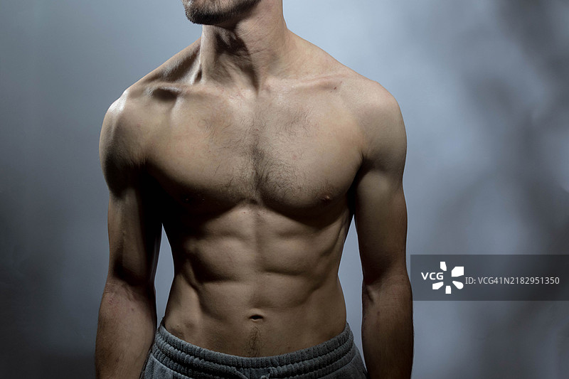 一位年轻男子赤裸上身，侧身望向灰色背景。图片素材