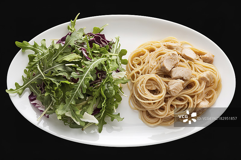 一盘新鲜的芝麻菜沙拉和一堆意大利面的照片，背景为黑色。图片素材