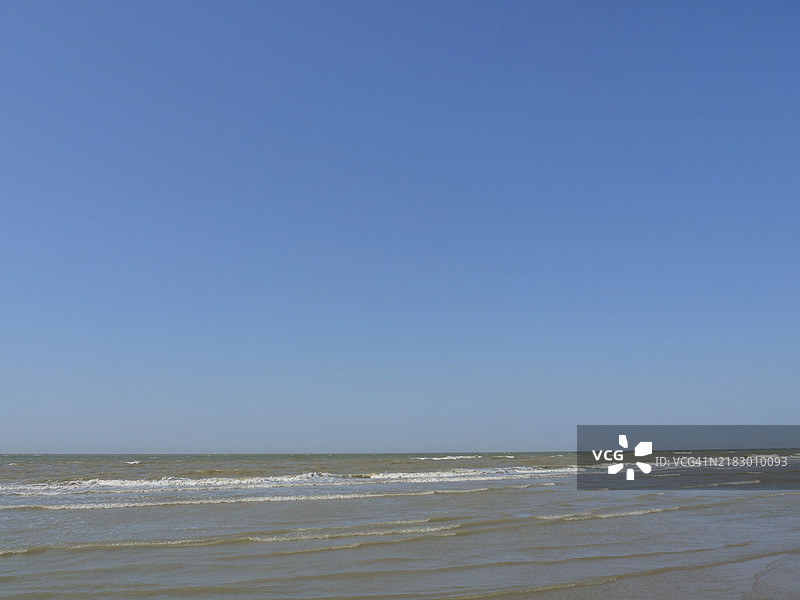 平静的海面和蓝天，轻柔的海浪，海边宽阔的沙滩上有海鸥，海滨长廊上的城市全景，德哈恩，比利时图片素材