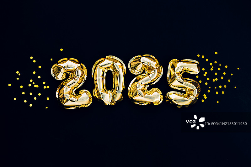 2025年新年假期贺卡。黑色背景上漂浮着金色箔气球和金色彩带。图片素材