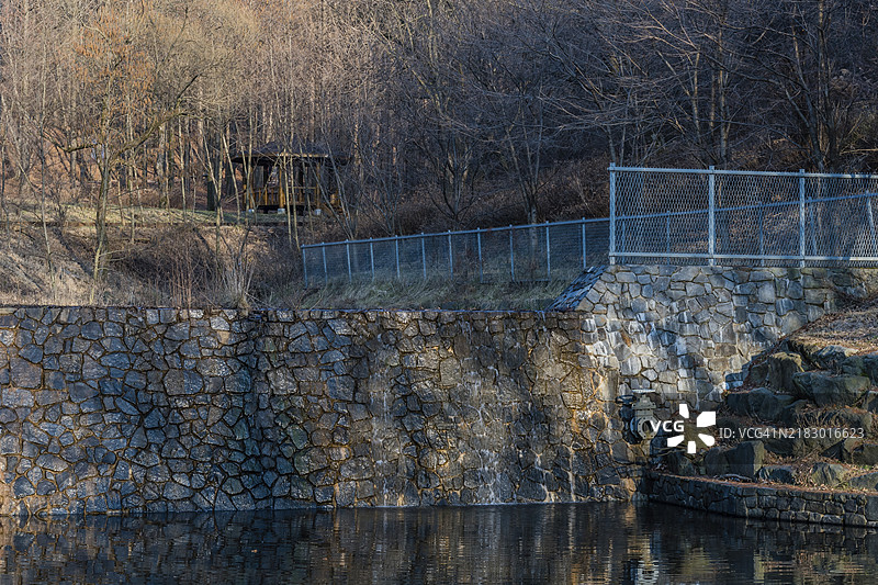被石墙围绕的池塘，水面平静，光秃的树木在水中倒影，位于韩国。图片素材