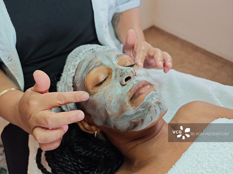 温和的泥土面膜在水疗中心的涂抹。图片素材
