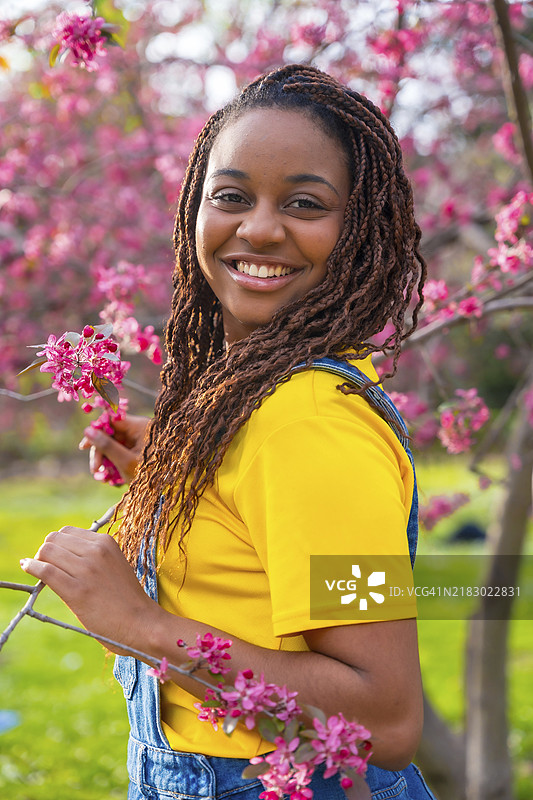 年轻非洲女性站在粉色花树旁的竖版肖像图片素材