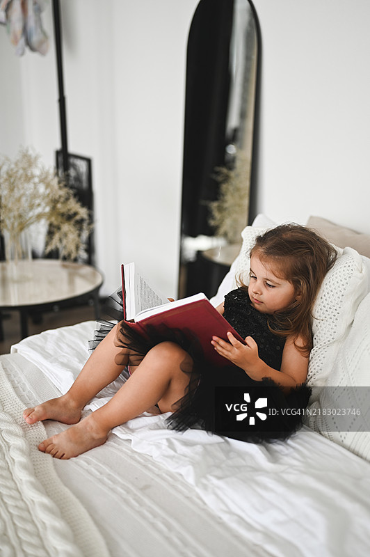 小女孩在床上读一本书。图片素材