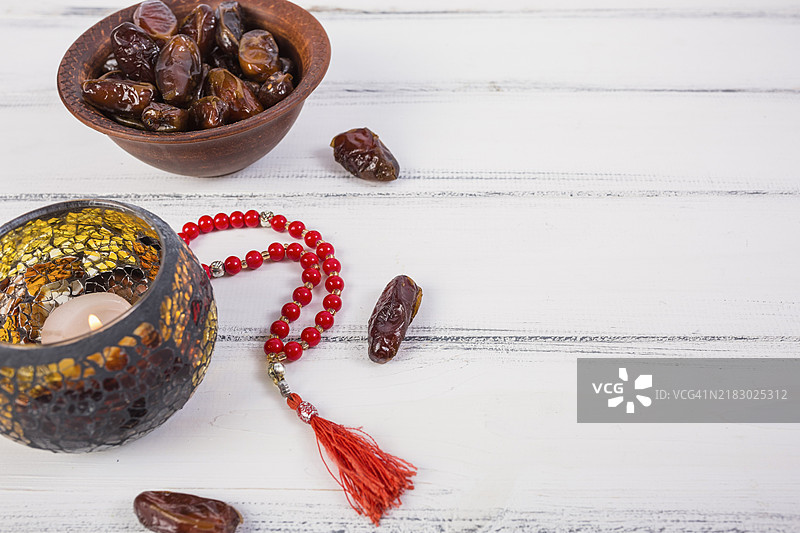 点燃的蜡烛与碗装多汁的枣子、红色祈祷珠子，白色木质背景图片素材