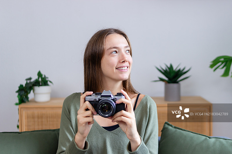 年轻的摄影师微笑着，手持一台复古相机，仰望着天空。图片素材