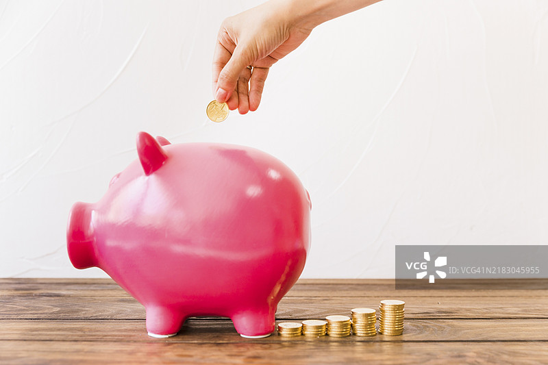 人手将硬币放入粉色储蓄罐图片素材