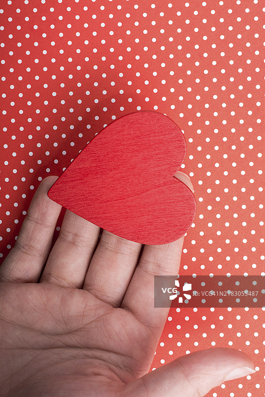 手中握着红色心形物体，背景是点状纸张图片素材