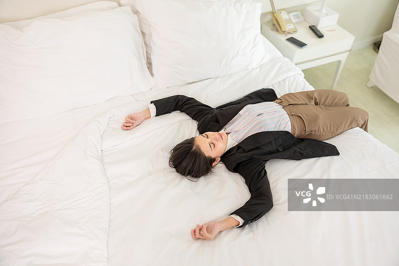 疲惫的女商人在酒店房间：过度劳累的商务旅行者在安静的私人空间中躺在床上，寻找宁静与舒适，以便在繁忙的商务旅行后恢复精力。图片素材