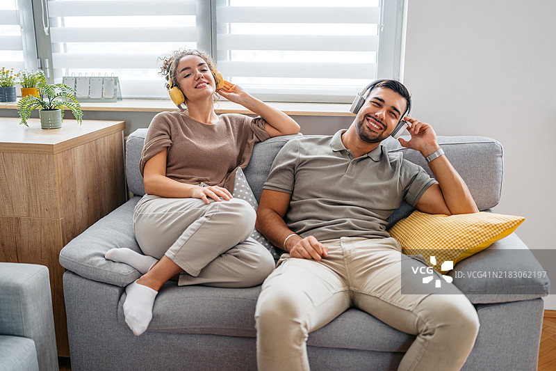 年轻情侣坐在家中房间里，戴着耳机听音乐图片素材