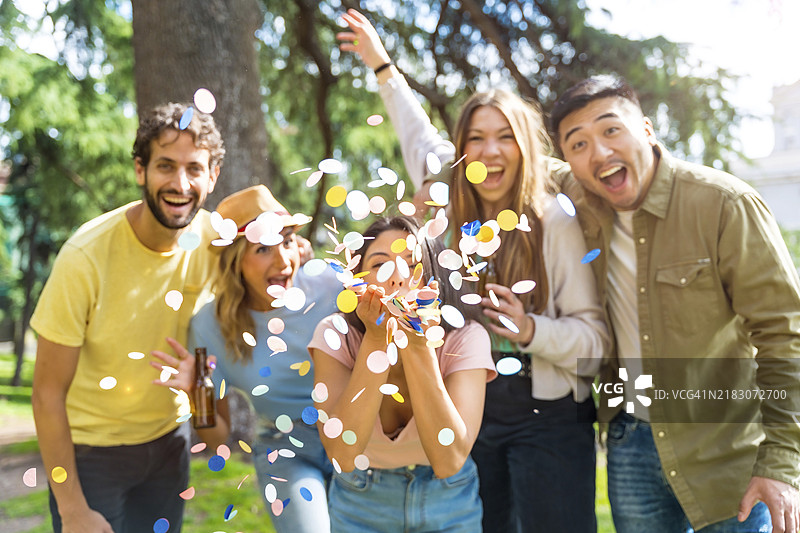 多种族的聚会人群在公园里欢笑抛洒五彩纸屑，享受与朋友们的乐趣图片素材