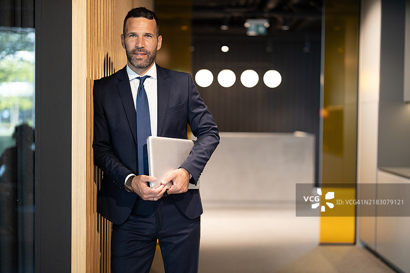 自信的首席执行官靠在现代办公室的墙上图片素材