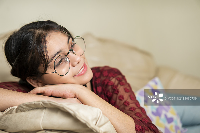 安静的印度女性躺在沙发上，面带灿烂的微笑，沉思着。图片素材