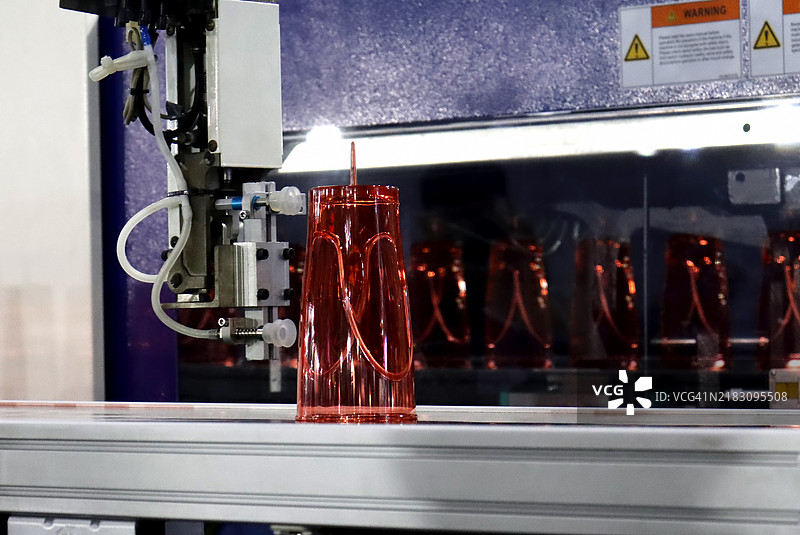 自动塑料注塑机的传送带上移动的聚丙烯杯子，配有机械手臂图片素材