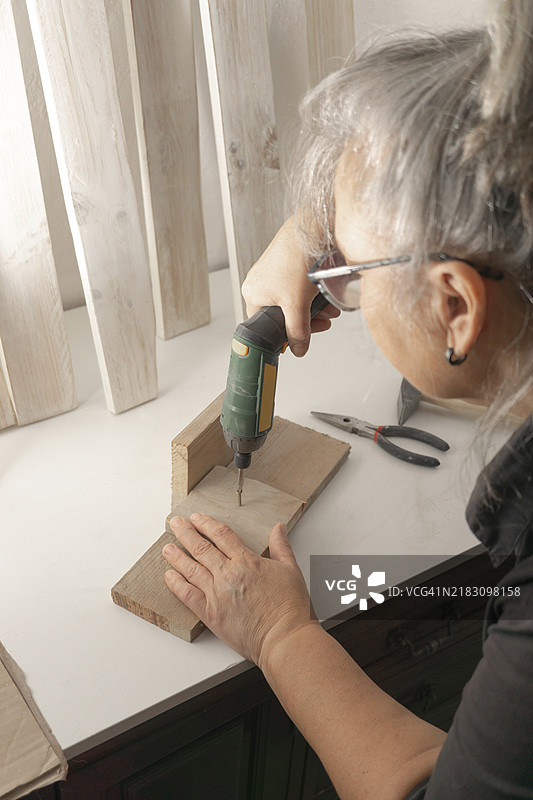 侧面看到一位女性正在用电动螺丝刀将螺丝拧入木头中图片素材