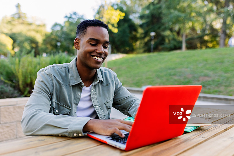 微笑的年轻黑人大学生在校园公园户外使用笔记本电脑学习图片素材