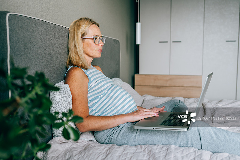 在线婴儿购物：一位怀孕的准妈妈在床上浏览选项图片素材