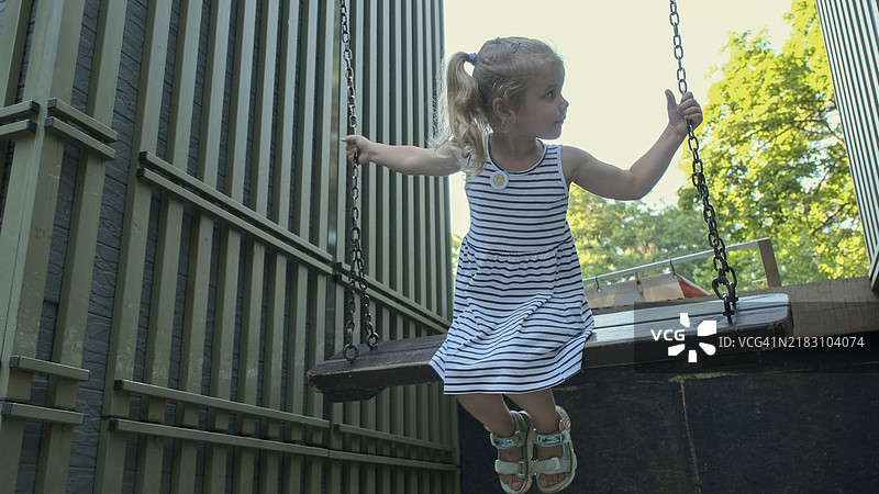 微笑的小女孩在秋千上荡秋千。特写镜头显示一位金发女孩在城市公园的秋千上荡秋千。乌克兰敖德萨。图片素材
