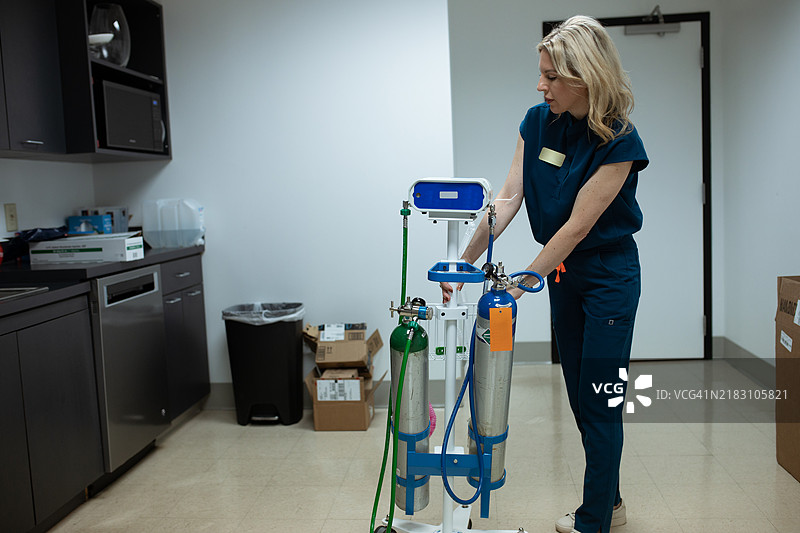 穿着医疗服的女性正在准备一种便携设备，该设备可以提供氧气和一氧化二氮的混合物以缓解疼痛。图片素材