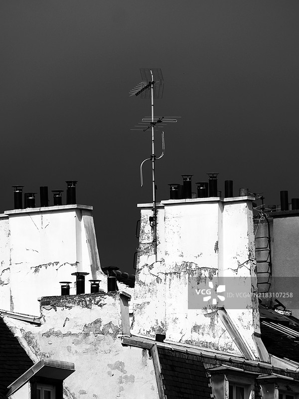 巴黎一栋老住宅楼屋顶的白色烟囱和耙形天线特写。阳光。灰色天空。自然铜绿。黑白色调。图片素材
