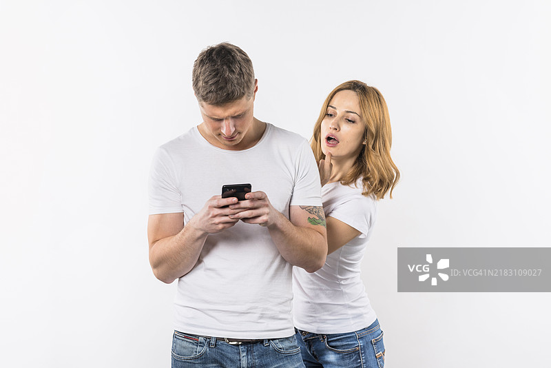 年轻女性在白色背景下窥视她男朋友的手机图片素材