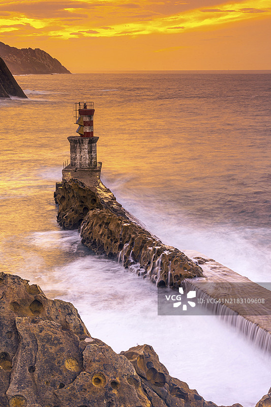 在吉普斯夸省的帕萨赫斯·圣胡安市灯塔下，橙色日落的长时间曝光。巴斯克地区图片素材