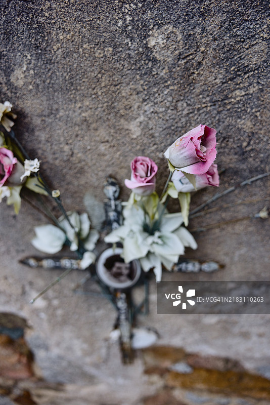 墓地中，撒丁岛巴里萨尔多的一个墓碑上，风化的墙壁后面摆放着人造玫瑰和十字架。图片素材