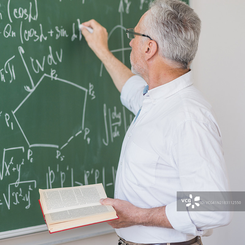 严肃的讲师戴着眼镜在黑板上写公式图片素材