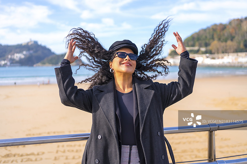时尚的拉丁女性穿着冬装，在海滩观景点整理她的头发图片素材