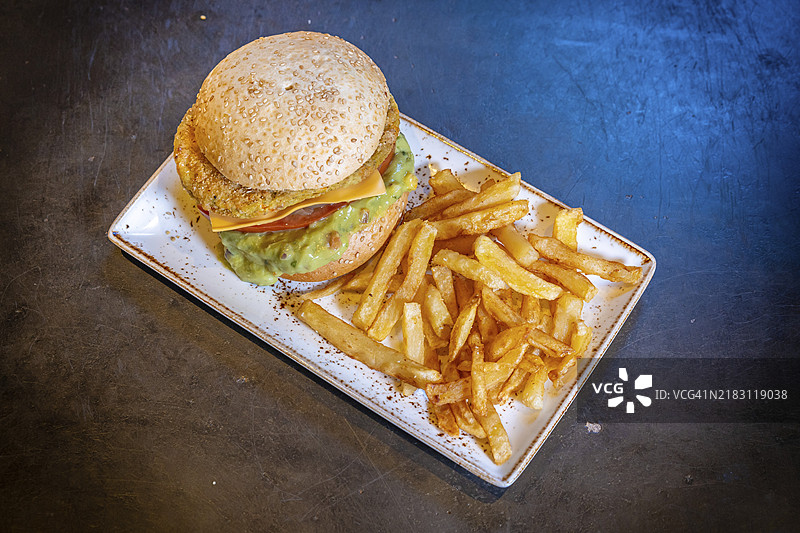 白盘上的素食汉堡配鳄梨酱和薯条，背景为黑色图片素材